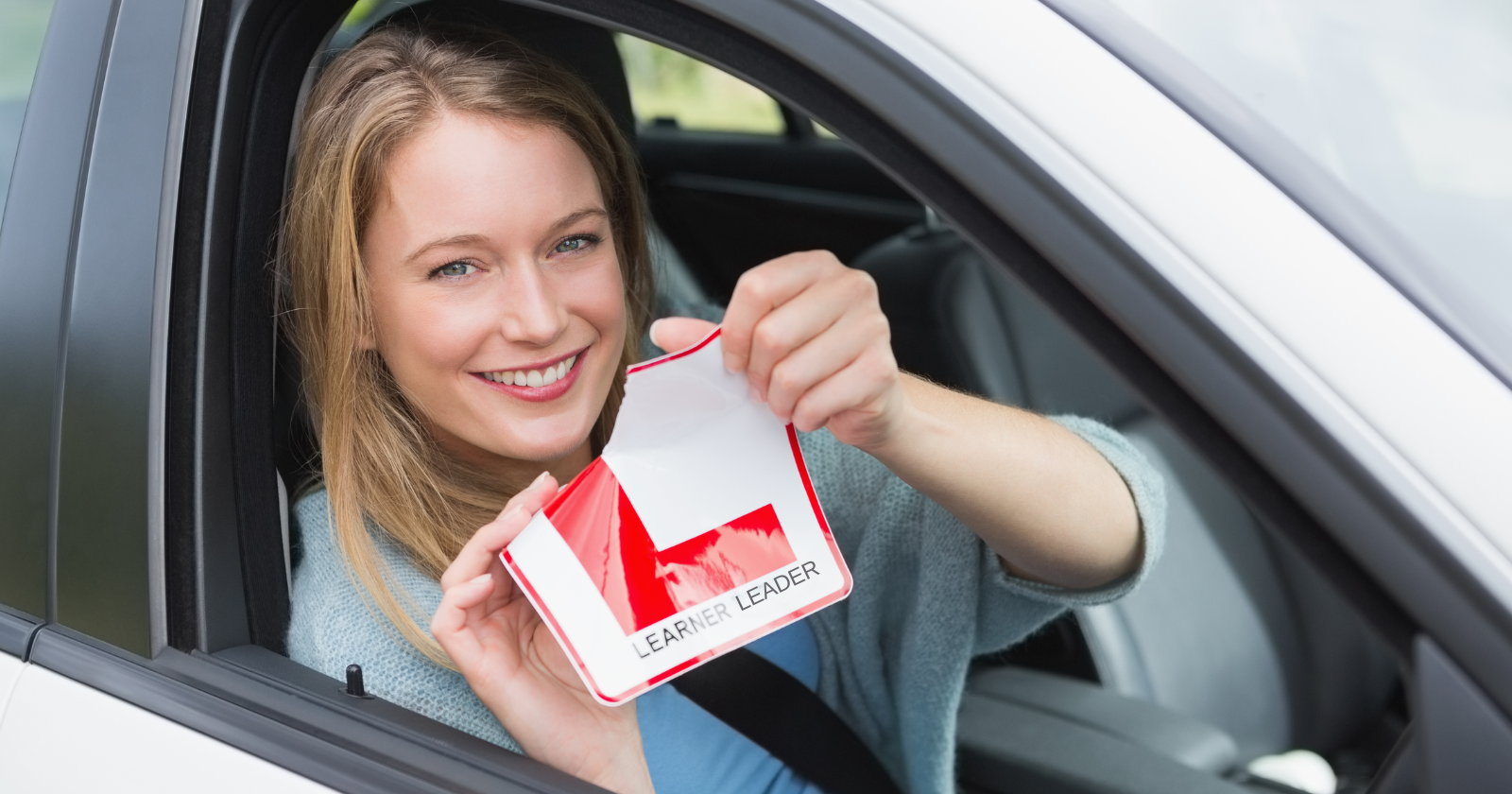 Woman in car ripping an L plate which says Learner Leader